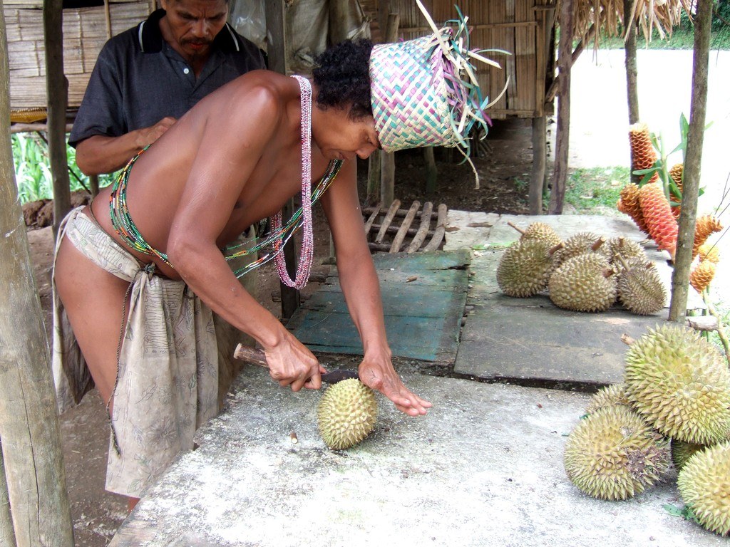 A worker opening a durian beside a pile of harvested fruit.