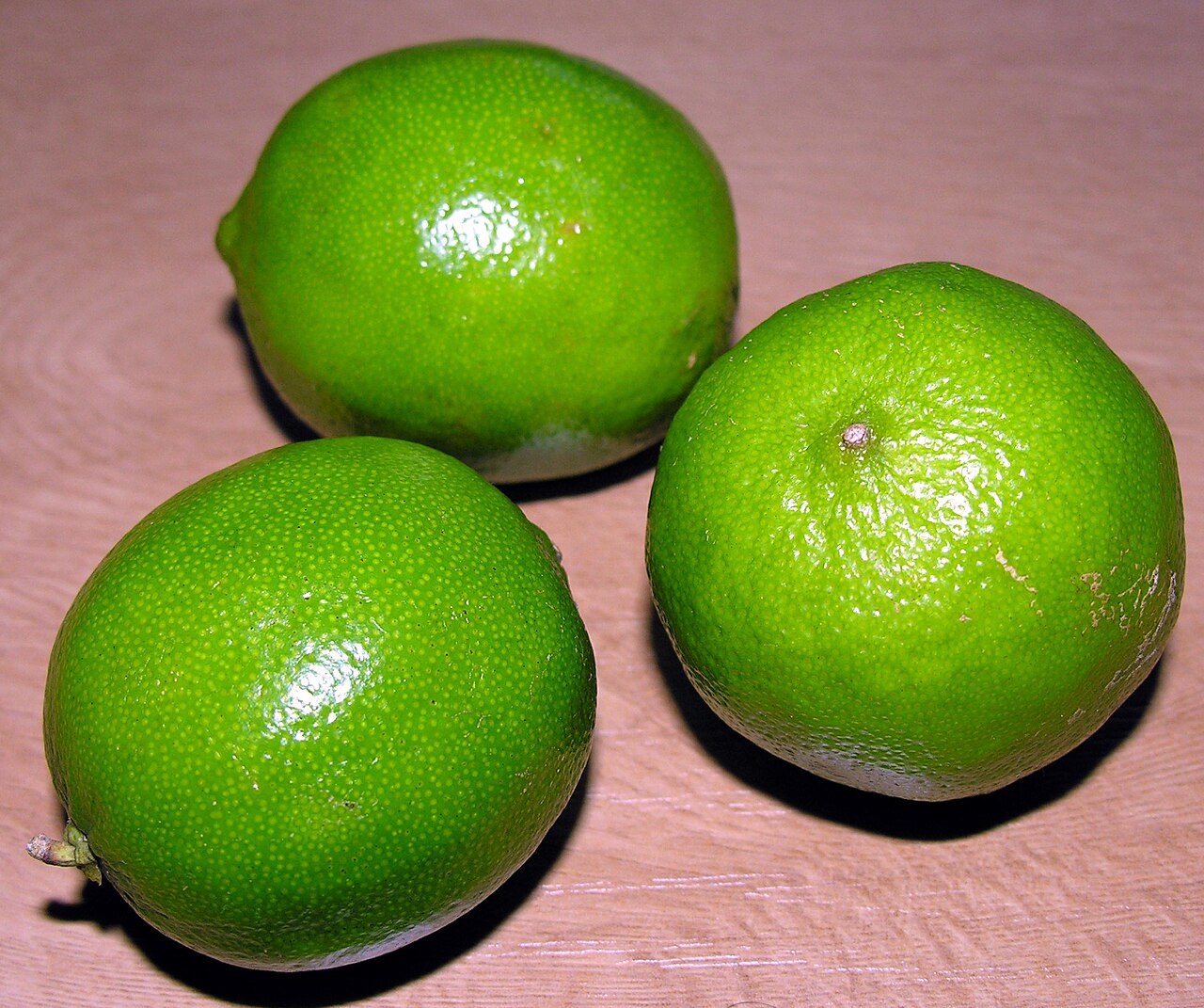 Three whole green limes on a plain surface.