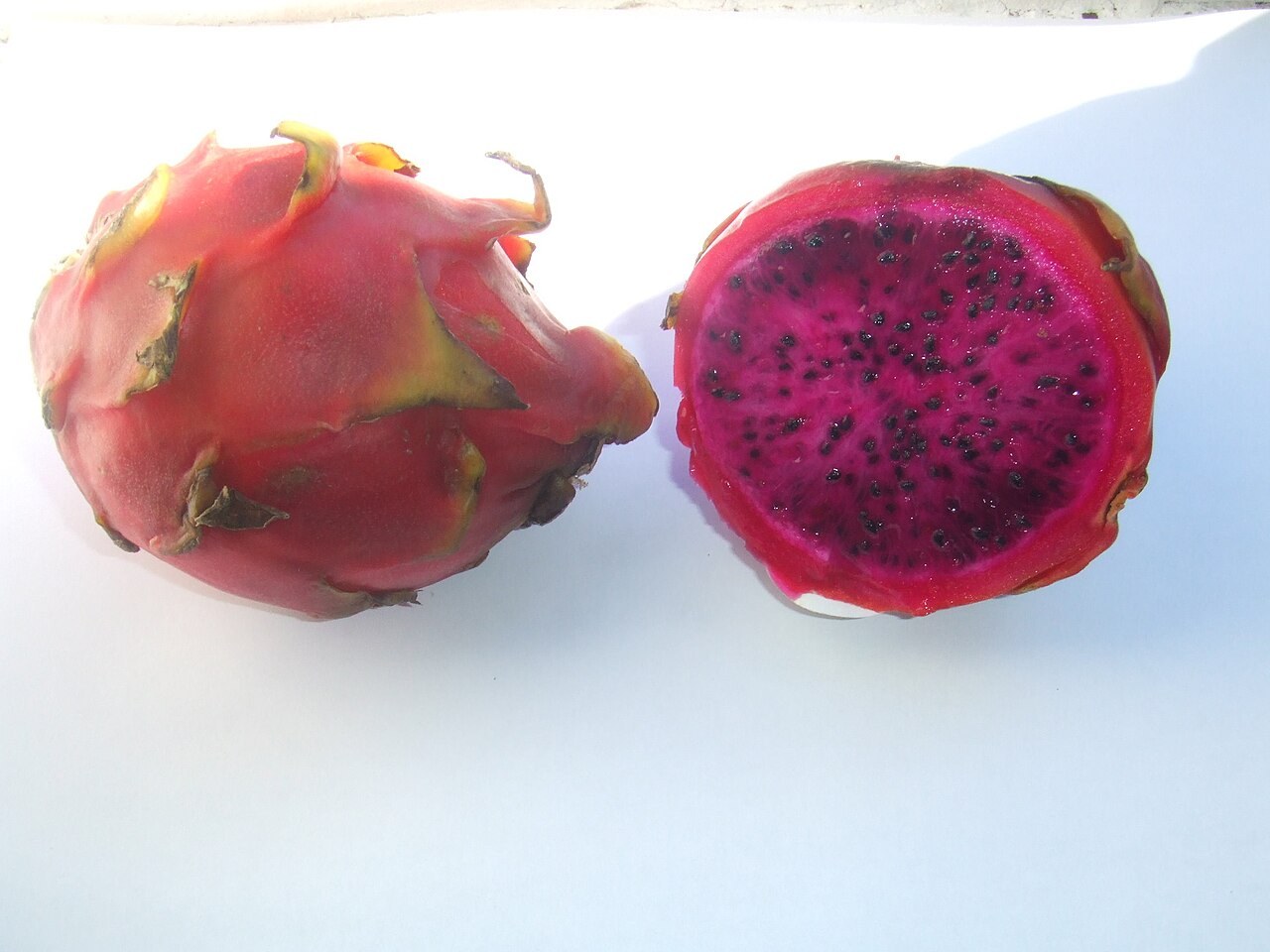 Whole and halved red-flesh dragon fruit on a light background.