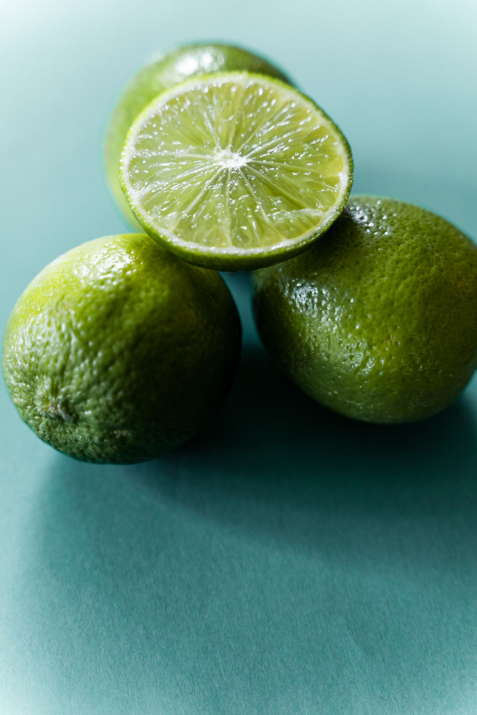 Whole green limes and a cut lime on a teal surface