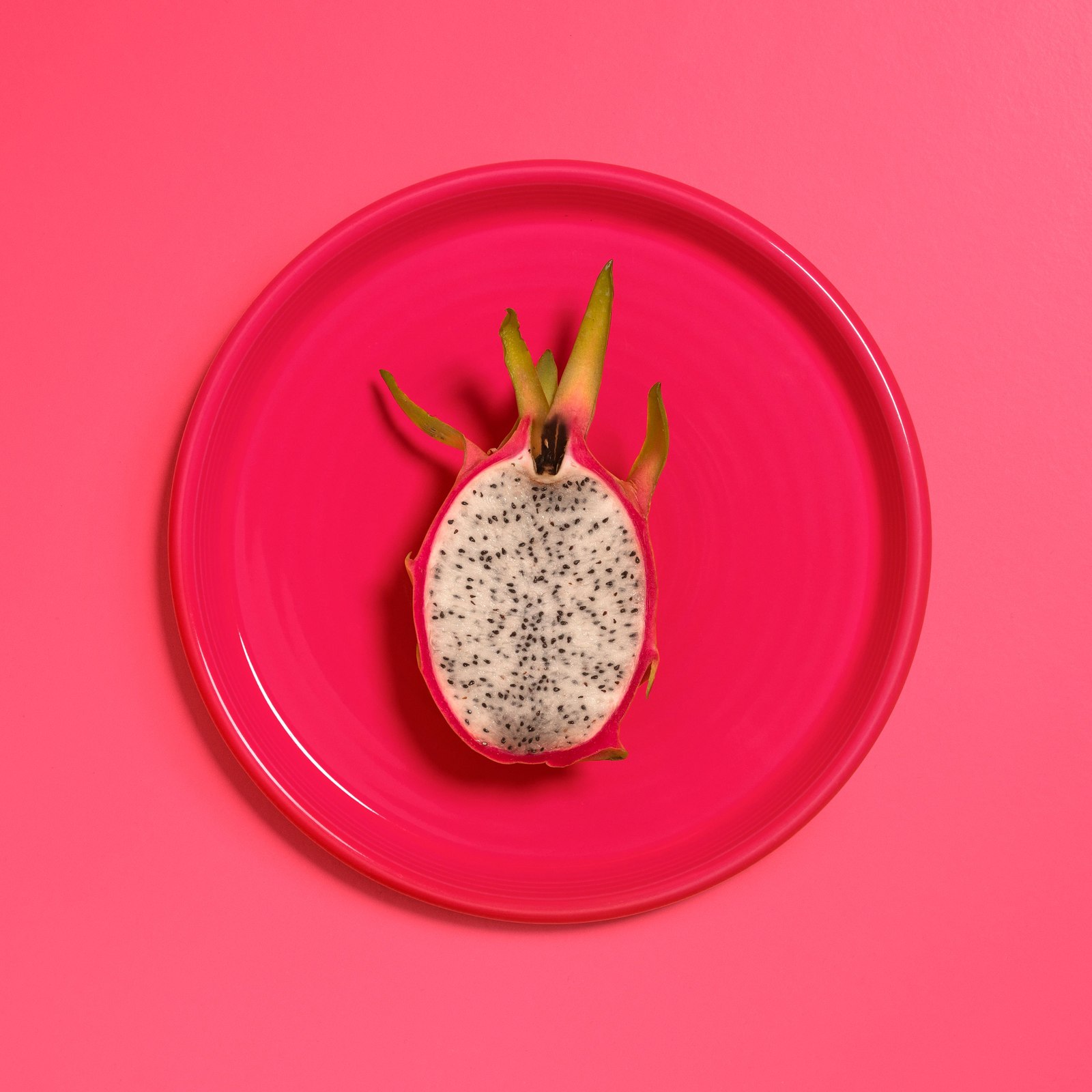 A halved white-flesh dragon fruit on a pink plate.
