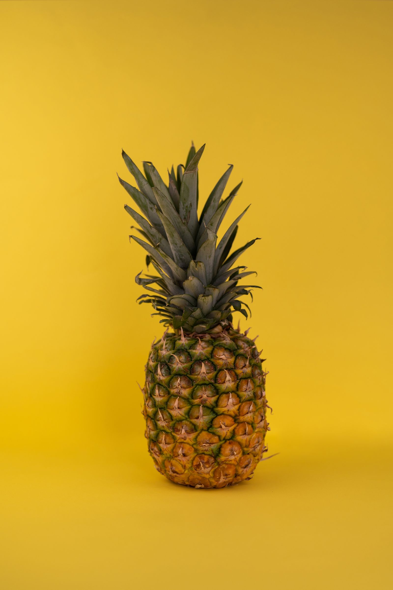 Whole pineapple with a green crown on a yellow background
