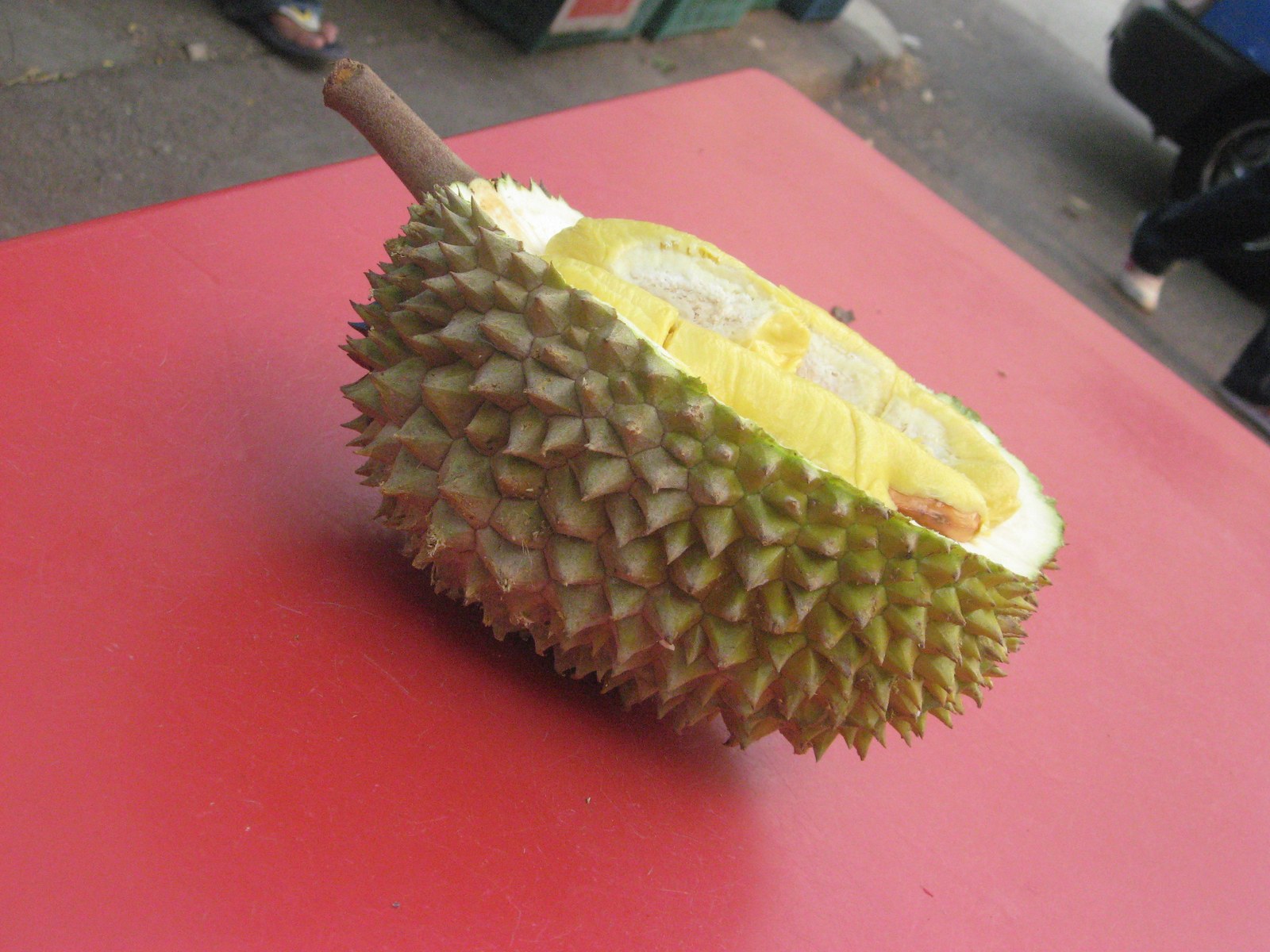 An opened durian with yellow flesh on a red counter.