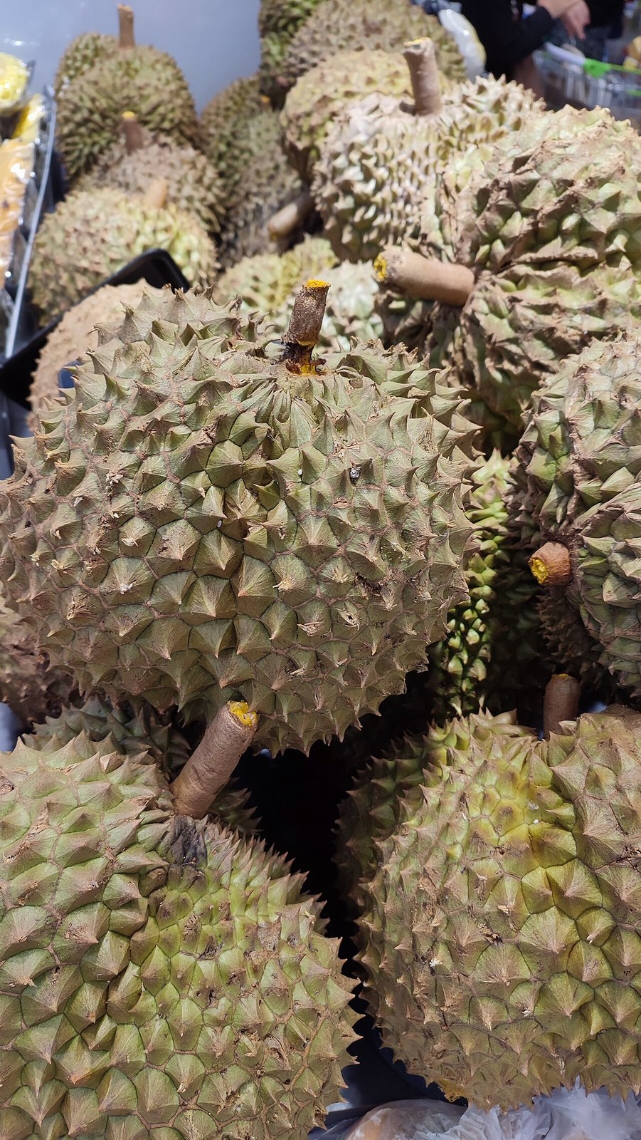 Whole thorny durians stacked at a market.