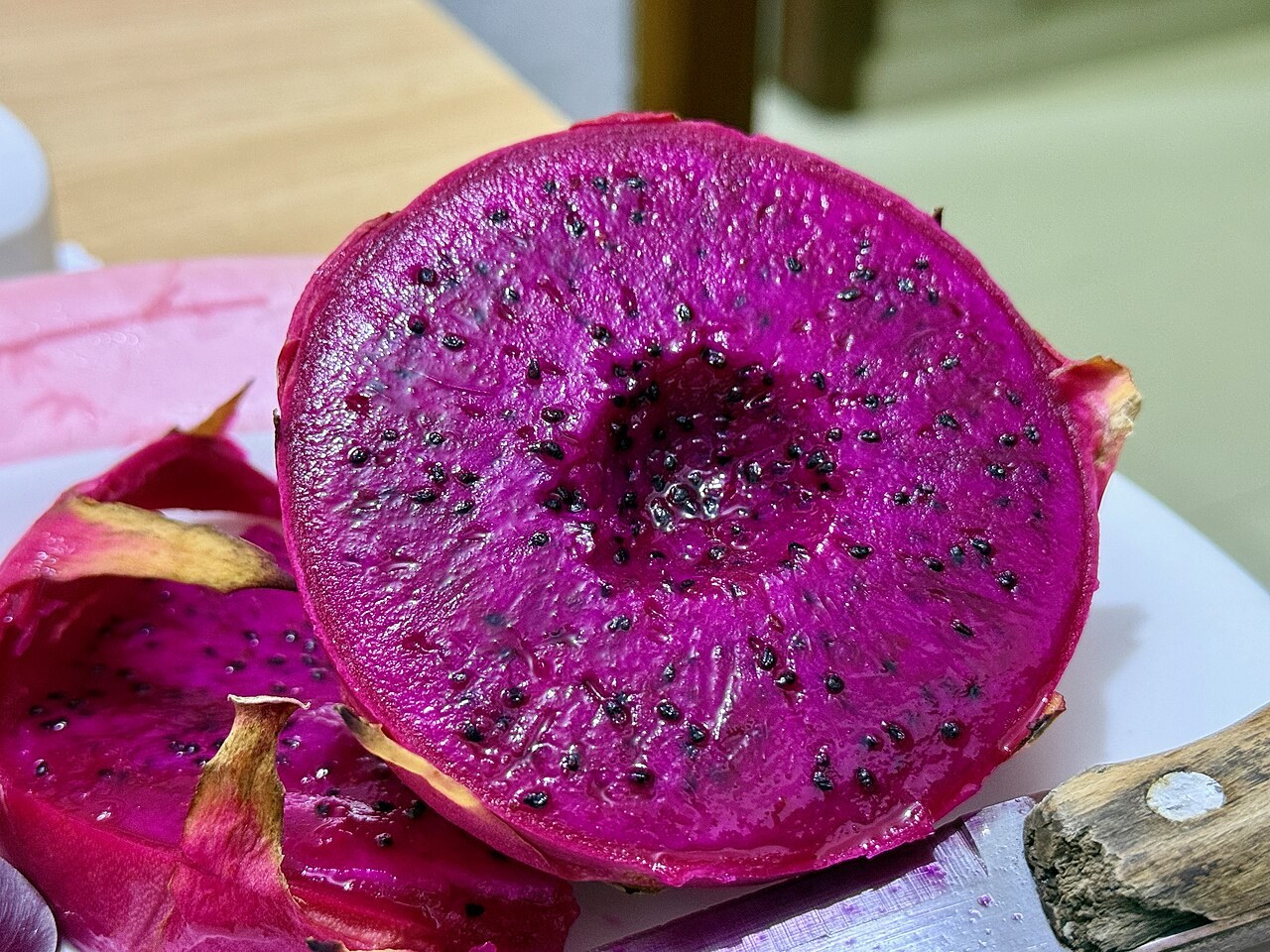 A red-flesh dragon fruit cut open on a cutting board beside a knife.