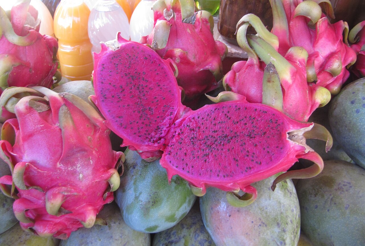 Red-flesh dragon fruit displayed with whole pink-skinned fruit at a market.