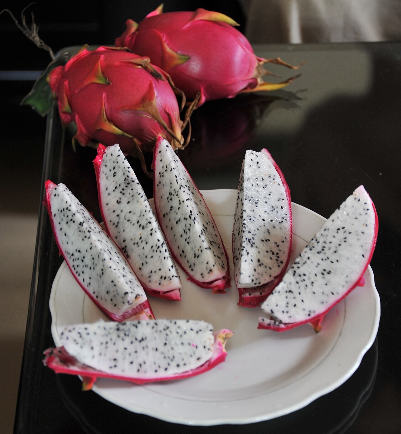 White-flesh dragon fruit wedges arranged on a white plate.
