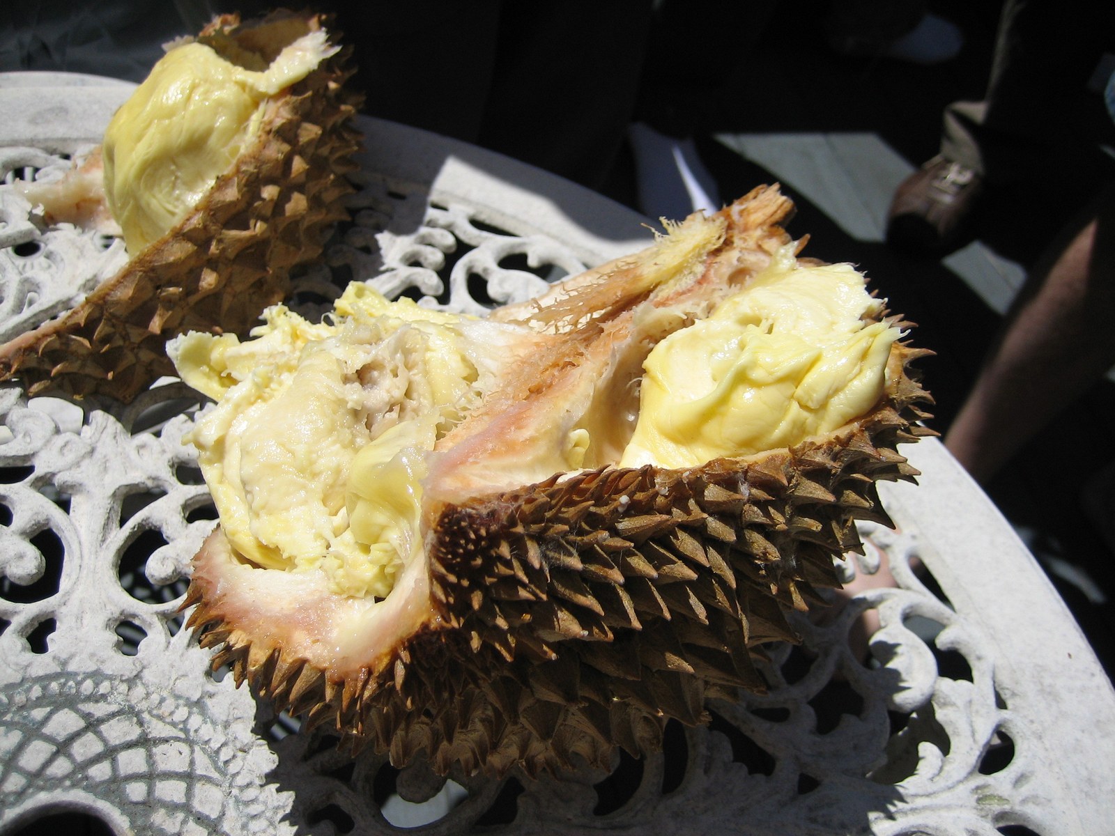 An opened durian showing pale yellow flesh on a white garden table.