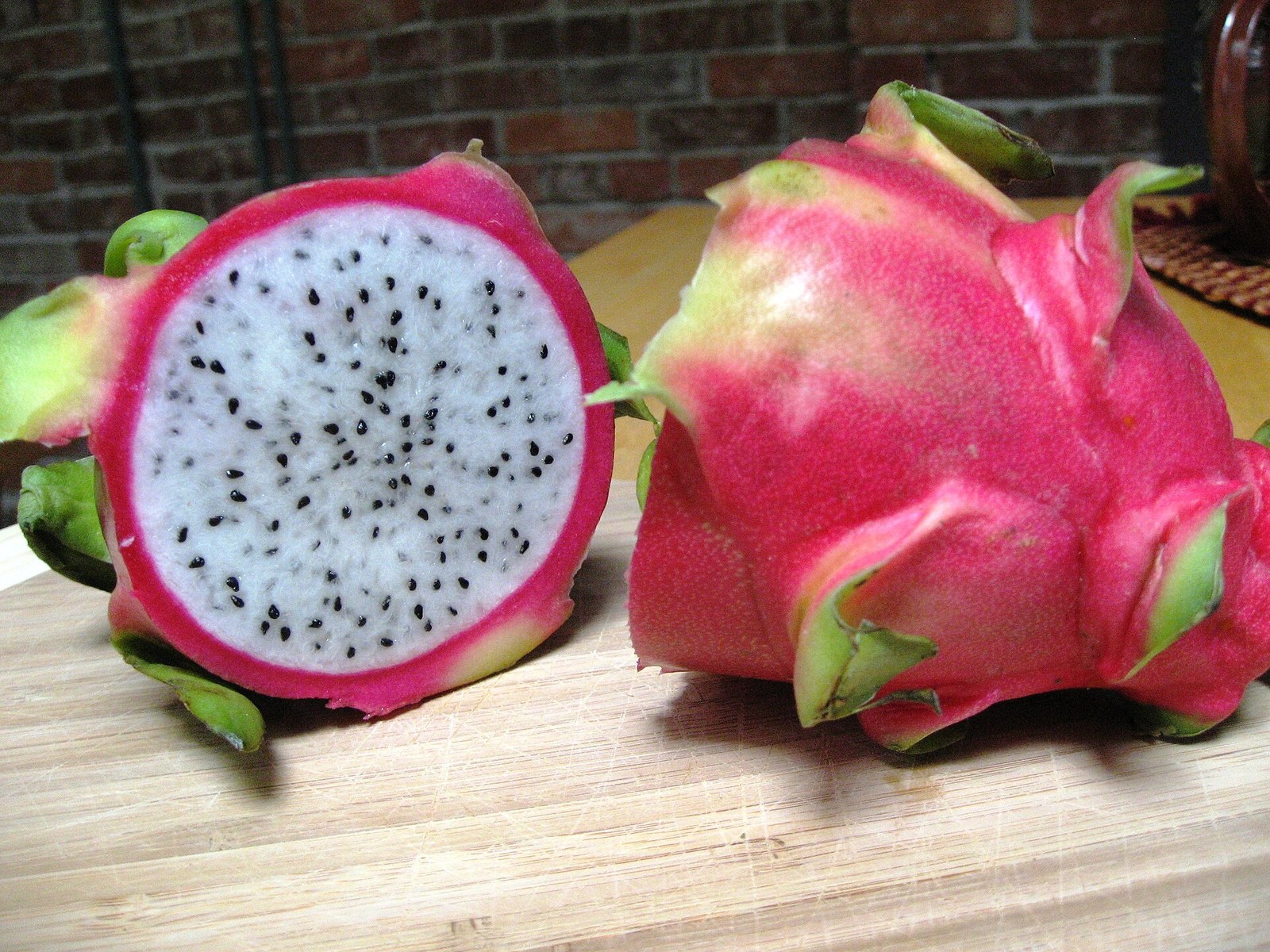 Whole and halved white-flesh dragon fruit on a wooden board.