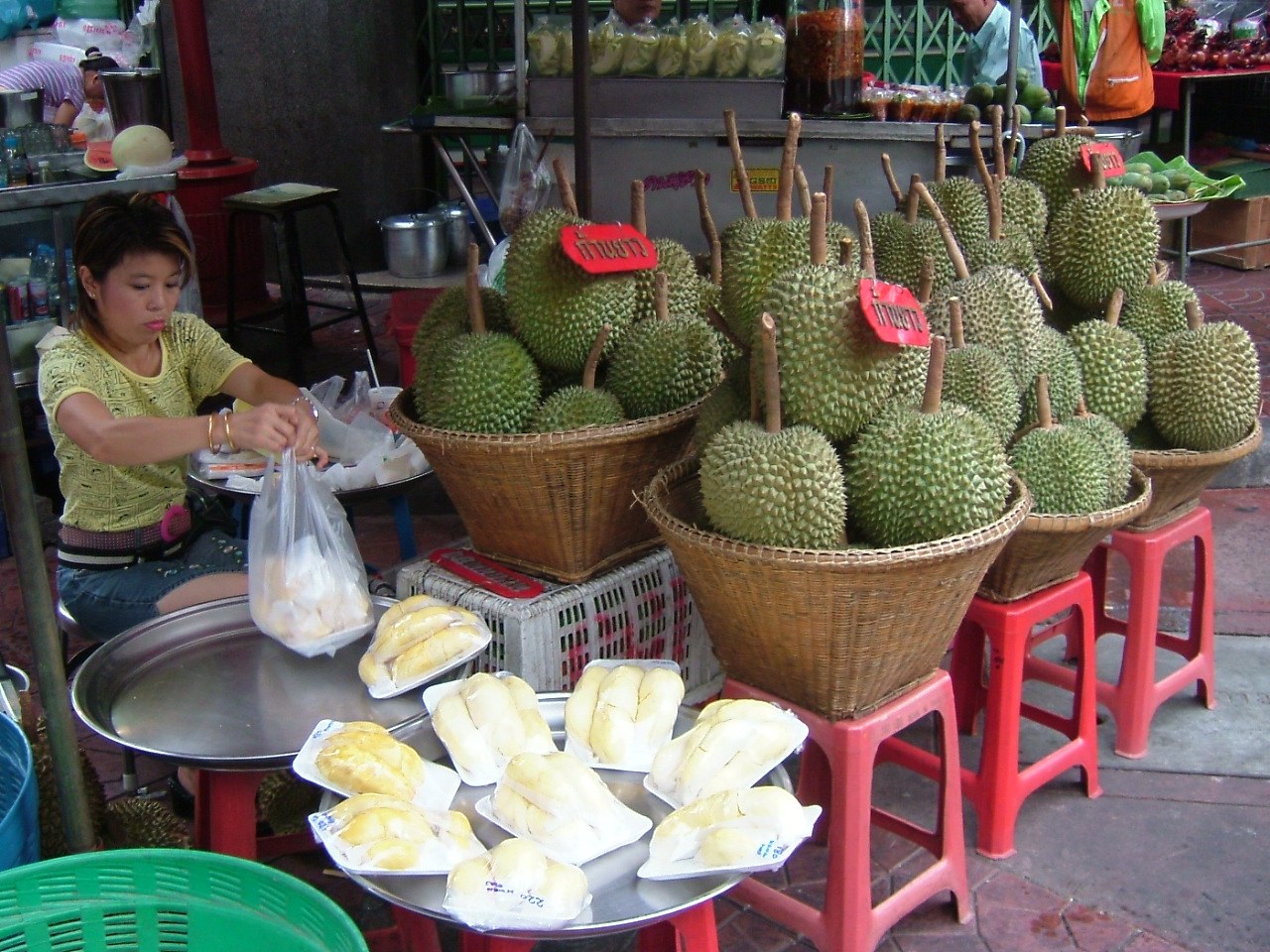 Whole durians in woven baskets beside fresh peeled durian at a market stall.