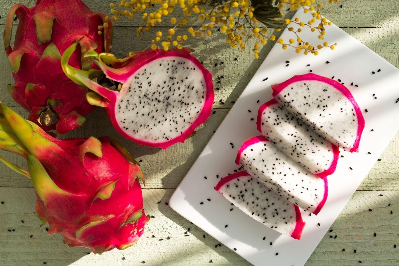 Whole and sliced white-fleshed dragon fruit on a ceramic plate