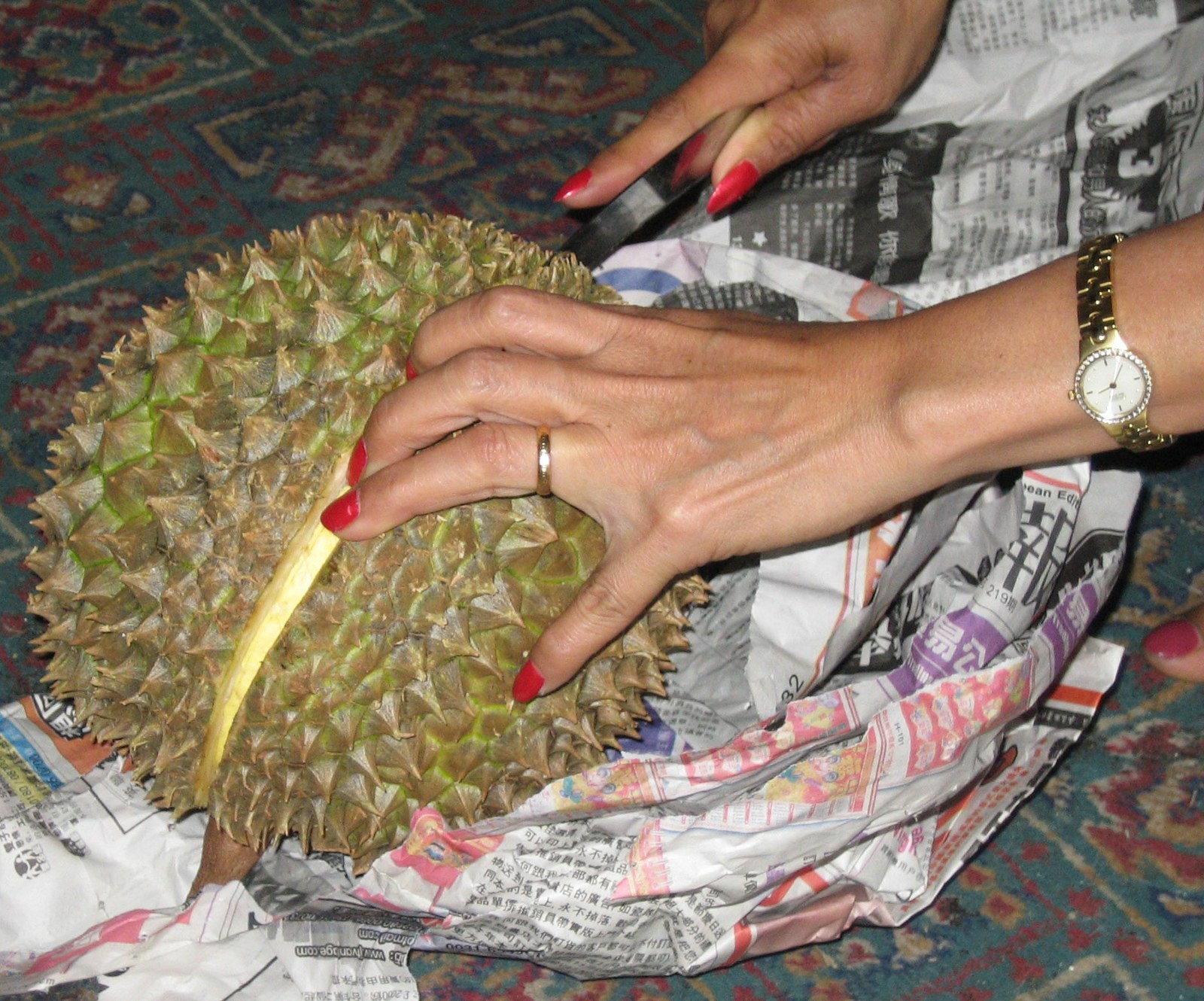 Hands use a knife to open a whole durian on newspaper.