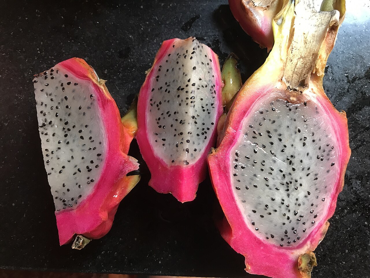 Three white-flesh dragon fruit halves on a dark surface.