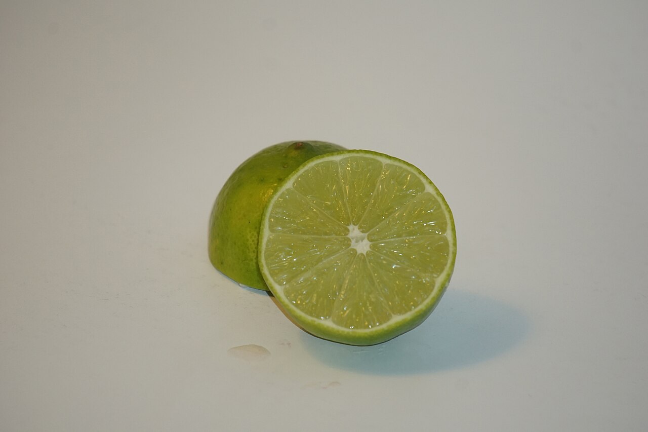 A whole and halved green lime on a plain background.