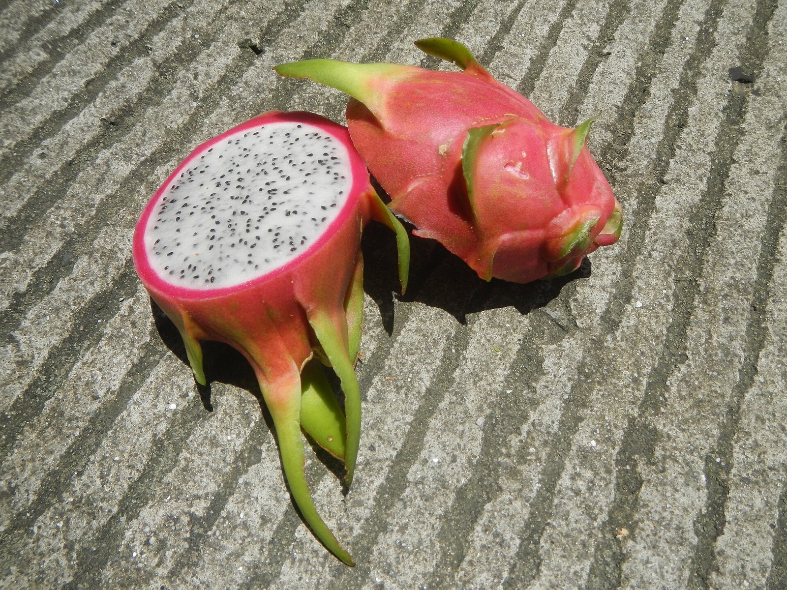 Whole and halved white-flesh dragon fruit on a textured surface.