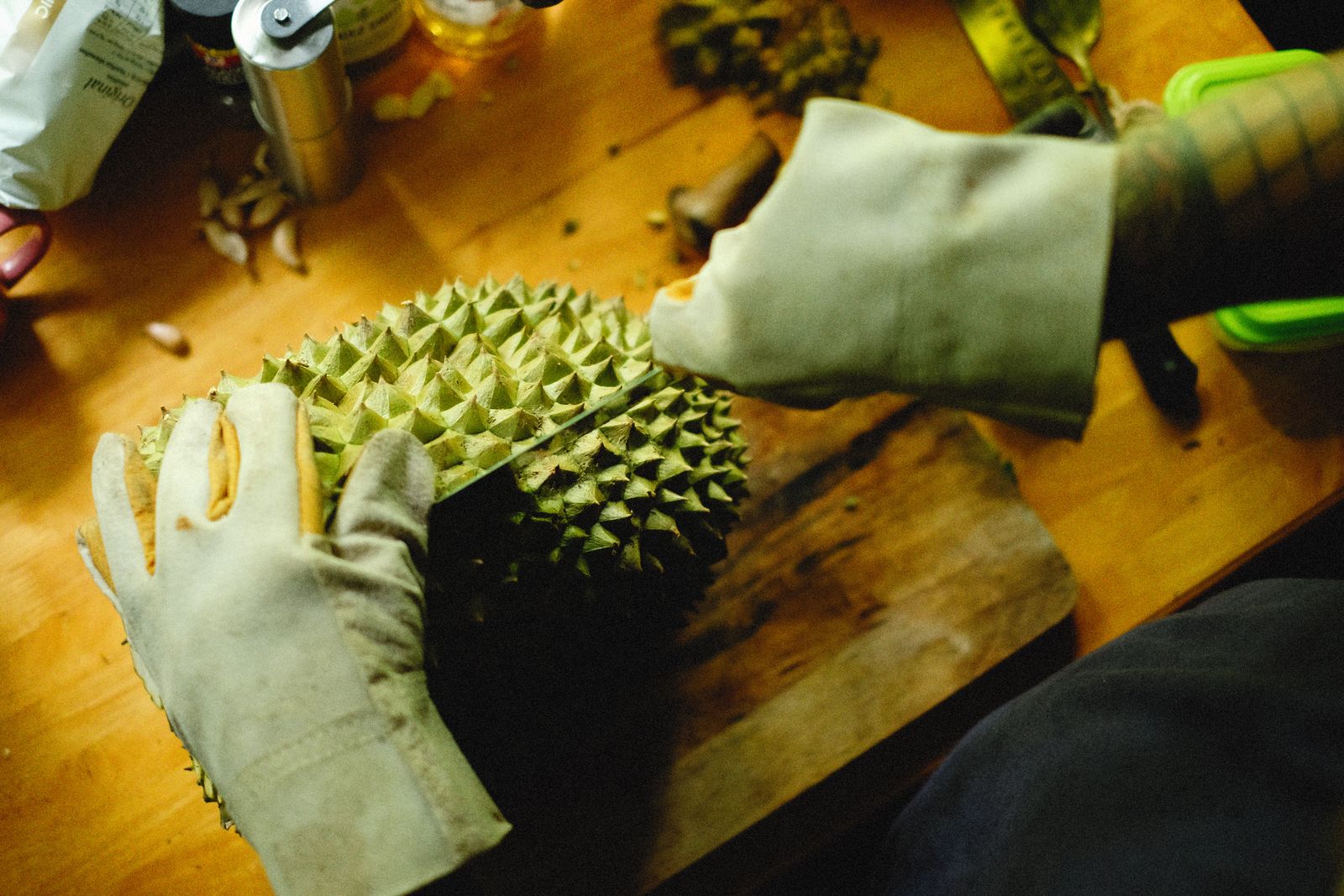 Gloved hands opening a durian on a wooden surface