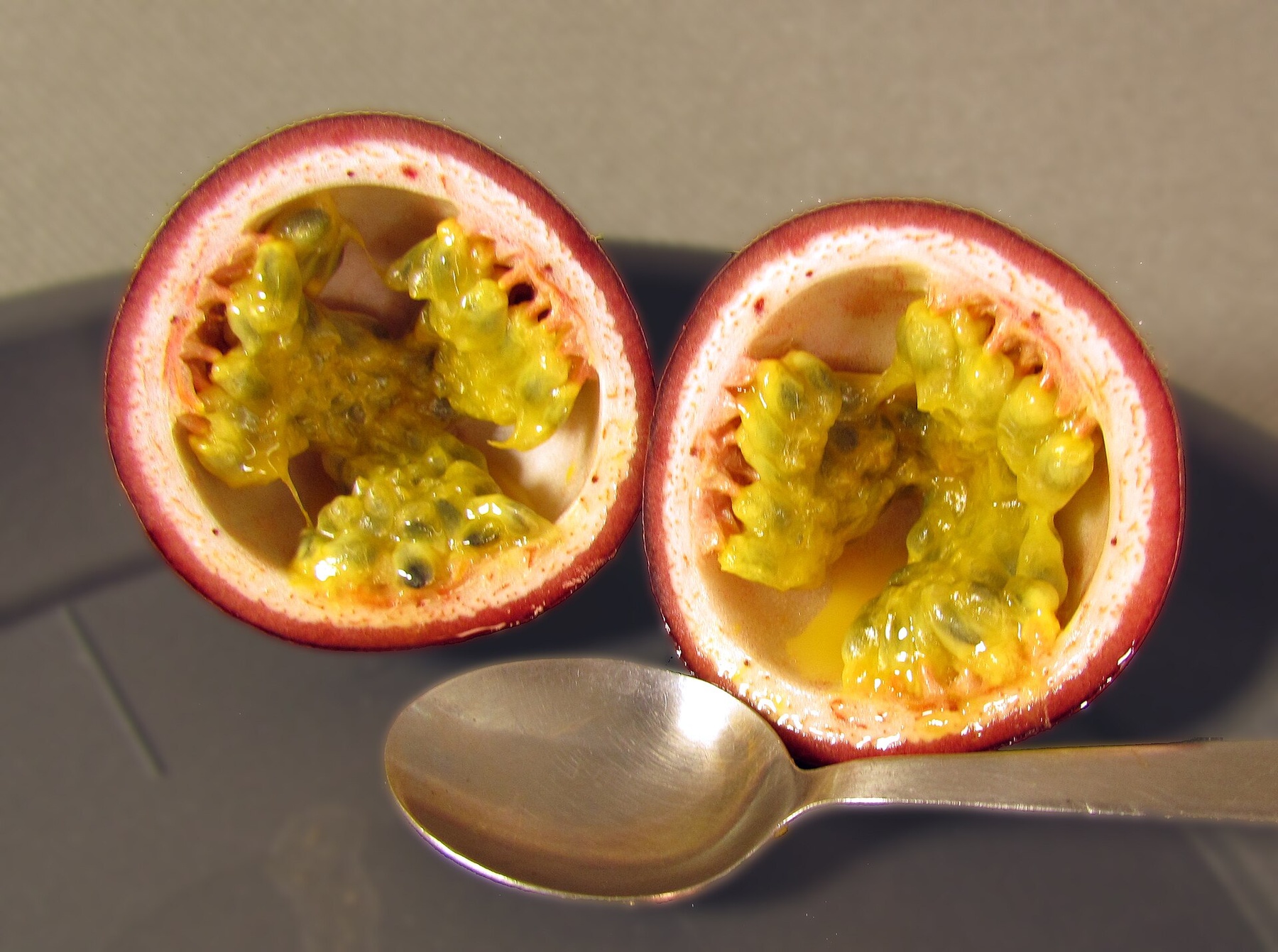 Two purple passion-fruit halves beside a spoon, with yellow pulp and dark seeds visible.