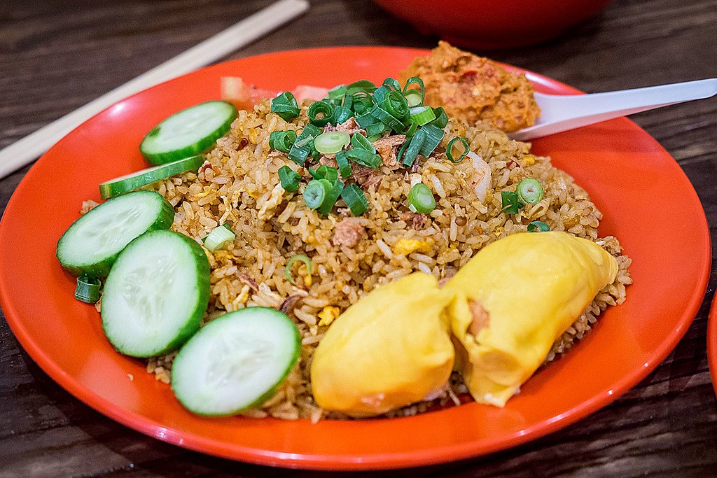 A plate of fried rice served with Musang King durian flesh and cucumber slices.