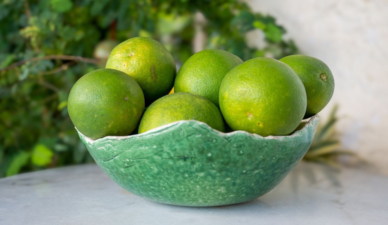 Whole green limes in a green ceramic bowl outdoors.