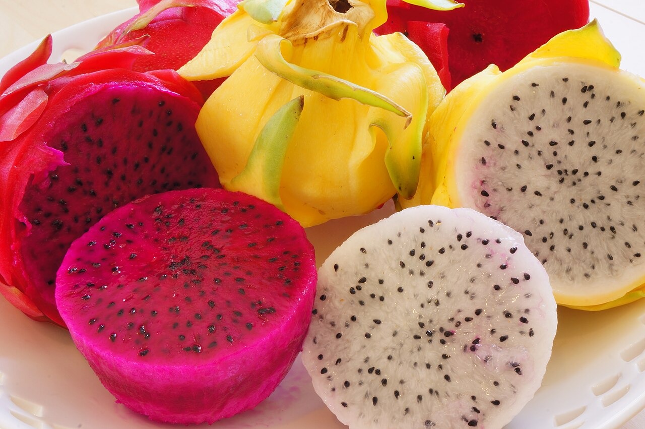 Cut dragon fruits showing white and red flesh beside yellow-skinned fruit.