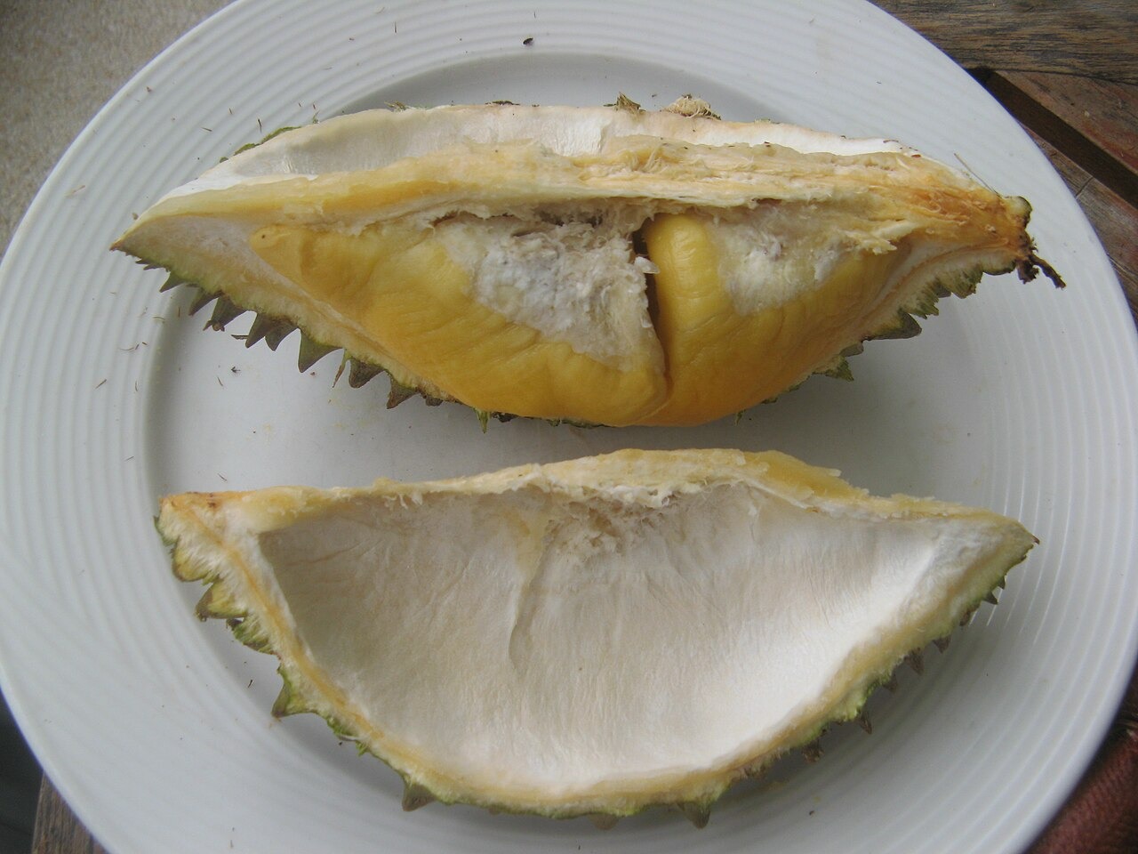 An opened durian with pale flesh arranged on a white plate.