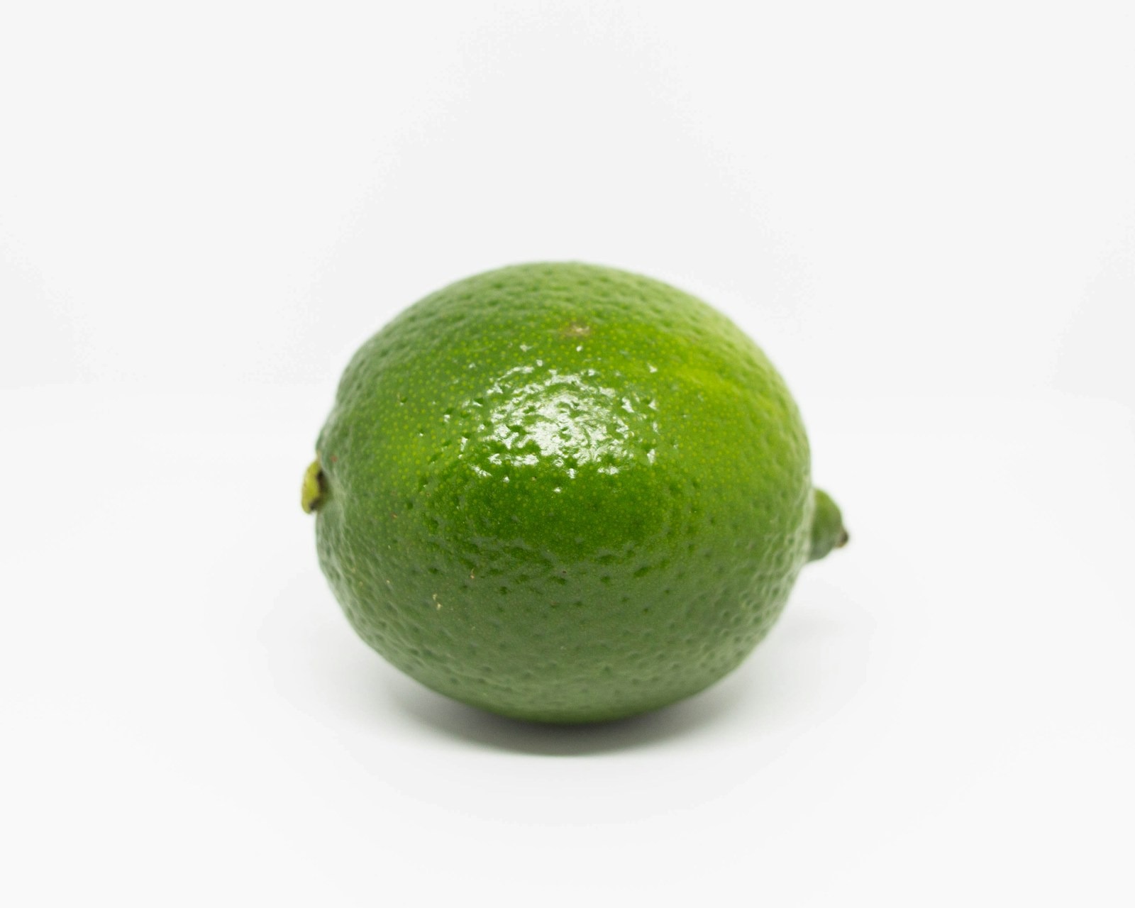 A whole green lime on a plain light background.