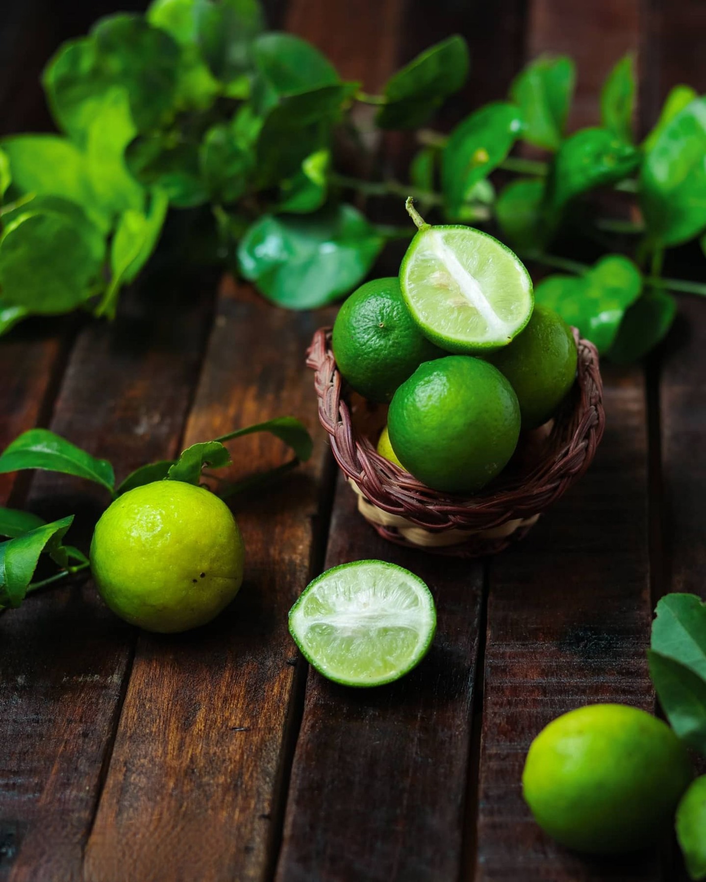 Whole and cut green limes arranged in a basket with foliage.
