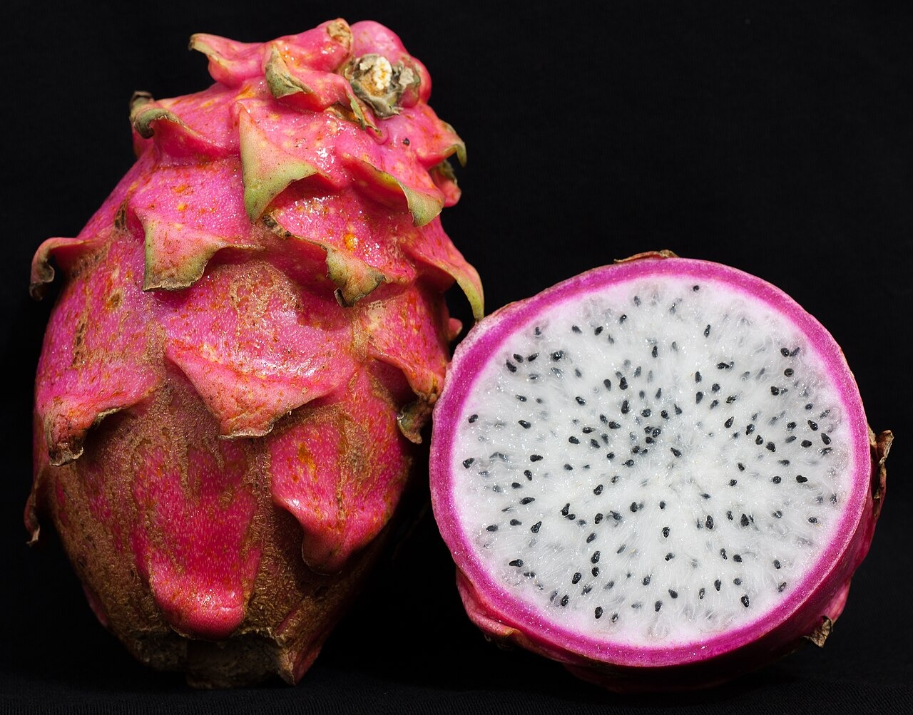 A whole dragon fruit beside a white-flesh half on a dark background.