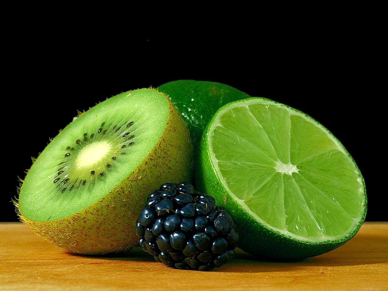 A cut lime displayed with kiwi and blackberries on a wooden surface.