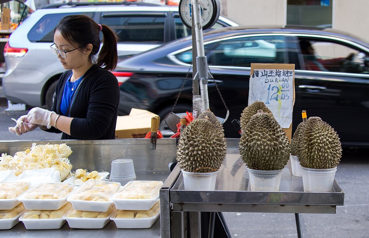 A market vendor preparing durian flesh beside whole fruit.