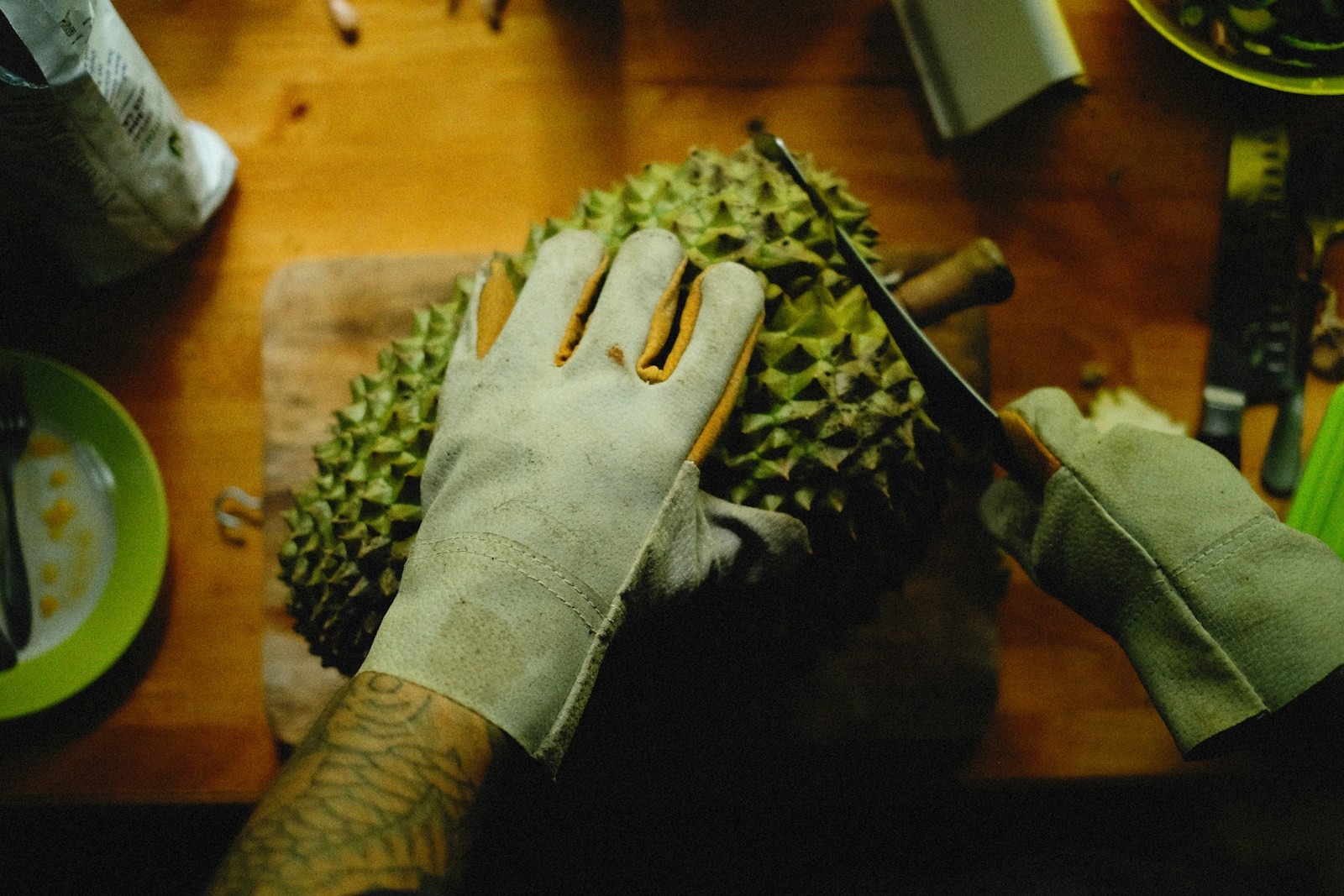 Gloved hands opening a whole durian on a work surface.