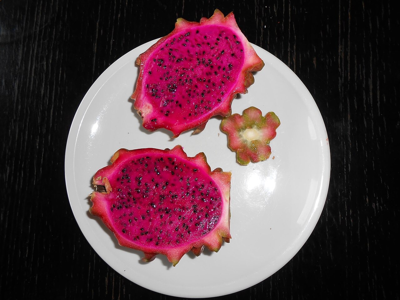 Red dragon fruit halves arranged on a white plate against a dark surface.